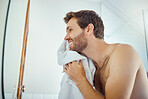One handsome man washing his face in a bathroom at home. Caucasian male using a towel to dry his face and looking in a mirror in his apartment.