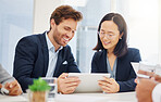 Two happy young diverse colleagues discussing plans and ideas together on a digital tablet device during a meeting in an office boardroom. Asian businesswoman and caucasian businessman brainstorming online with smart apps