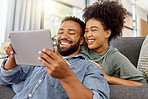 Mixed race couple smiling while using a digital tablet together at home. Joyful hispanic boyfriend and girlfriend laughing while relaxing and using social media on a digital tablet in the lounge at home
