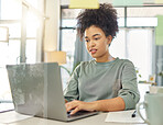 Young mixed race woman working a laptop sitting at a table at home. One focused hispanic female with a curly afro planning and typing an email alone in the lounge at home