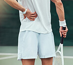 Rearview unknown mixed race tennis player suffering from backache in court game. Hispanic fit athlete in pain while holding and rubbing back injury in match. Sporty man standing alone in sports club