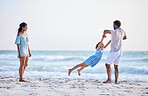 Happy mixed race family enjoying family time together at the beach. Loving father spinning his daughter by the arms and having fun by the sea while her mother watch. Young couple enjoying vacation by the beach with their little girl