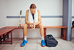 Young squash player sitting in a locker room waiting for his match. Caucasian player taking a break and thinking in his gym. Squash player sitting with his racket and bag before a match.