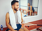 Young player drinking water while talking to his friend. Two friends bonding after a squash match. Two men sitting in a gym locker room after a match. Confident friends being social at the gym