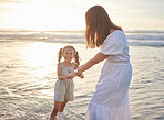 Cute little girl and her mixed race mother playing in the water at the beach. Young daughter and her mom spending quality time together by the ocean during the summer. Happy and playful at sunset