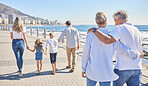 Rear view of a senior couple strolling on a seaside promenade while their children and grandchildren walks ahead.