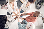 Group of five diverse businesspeople piling their hands together in an office at work. Business professionals having fun standing with their hands stacked for support and unity from above