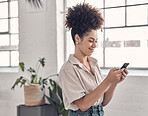 Young cheerful mixed race businesswoman typing a message on a phone at work. One creative hispanic female businessperson with a curly afro using social media on her cellphone in an office