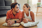 Loving young caucasian couple looking at each other and laughing while lying on the living room floor with cushions. Couple spending time and happy to be together