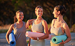 Beautiful yoga women bonding and holding yoga mats in outdoor practice in remote nature. Diverse group of young smiling active friends standing together. Three happy people getting ready to be mindful