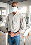 Young african american businessman standing in an office wearing a mask at work. Male business professional wearing a mask protecting from a virus and standing in an office at work