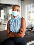 Young african american businesswoman standing with her arms crossed and wearing a mask at work. One confident black female boss wearing a mask protecting from a virus and standing at work