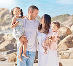 A happy mixed race family of four enjoying fresh air at the beach. Hispanic couple bonding with their daughters while standing and carrying their daughters