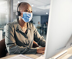 One african american call centre telemarketing agent wearing face mask as health and safety protocol talking on headset while using computer in an office. Female consultant operating helpdesk for customer service and sales support during covid pandemic