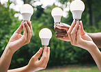 Multiple hands holding lightbulbs outside in nature. Closeup of multiethnic people holding bulbs as a concept of sustainable electricity. Multiracial people holding lightbulbs
