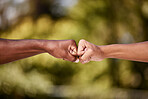 Closeup of men doing a fist bump against a blur background. Two male hands and arms punch together for interracial friendship, brotherhood and unity concept