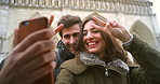 Excited young couple making the peace sign and taking a selfie on a cellphone