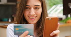 Smiling woman making an online booking on her smartphone using a debit card