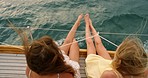 Two women swinging their feet from the side of a yacht during a cruise seen from above. Two friends enjoying a yacht cruise swinging their feet from the side of the boat