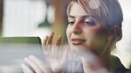 Content young businesswoman sitting by a window in a cafe using her digital tablet. Young woman using a wireless tablet while sitting in a cafe. Young businesswoman thinking while using her tablet