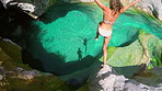 Happy young woman in white bikini jumping from cliff swimming in a lake. Two people jumping into a lake to swim. Young woman looking at her friend after jumping into a lake to swim
