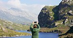 Rear view of a young woman using a smartphone to take a picture of a mountain. Unrecognizable woman taking a picture with her phone while hiking through nature on an adventure travel vacation