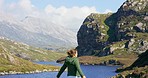 Rear view of a young woman standing with open arms, celebrating life. Unrecognizable woman enjoying the mountain view while hiking through nature on an adventure travel vacation